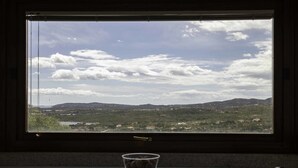 A window with a view of a landscape, a table with a glass, and a chair.