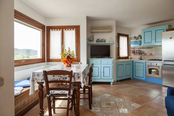 A kitchen with blue cabinets, a dining table with chairs, a TV, and a refrigerator.