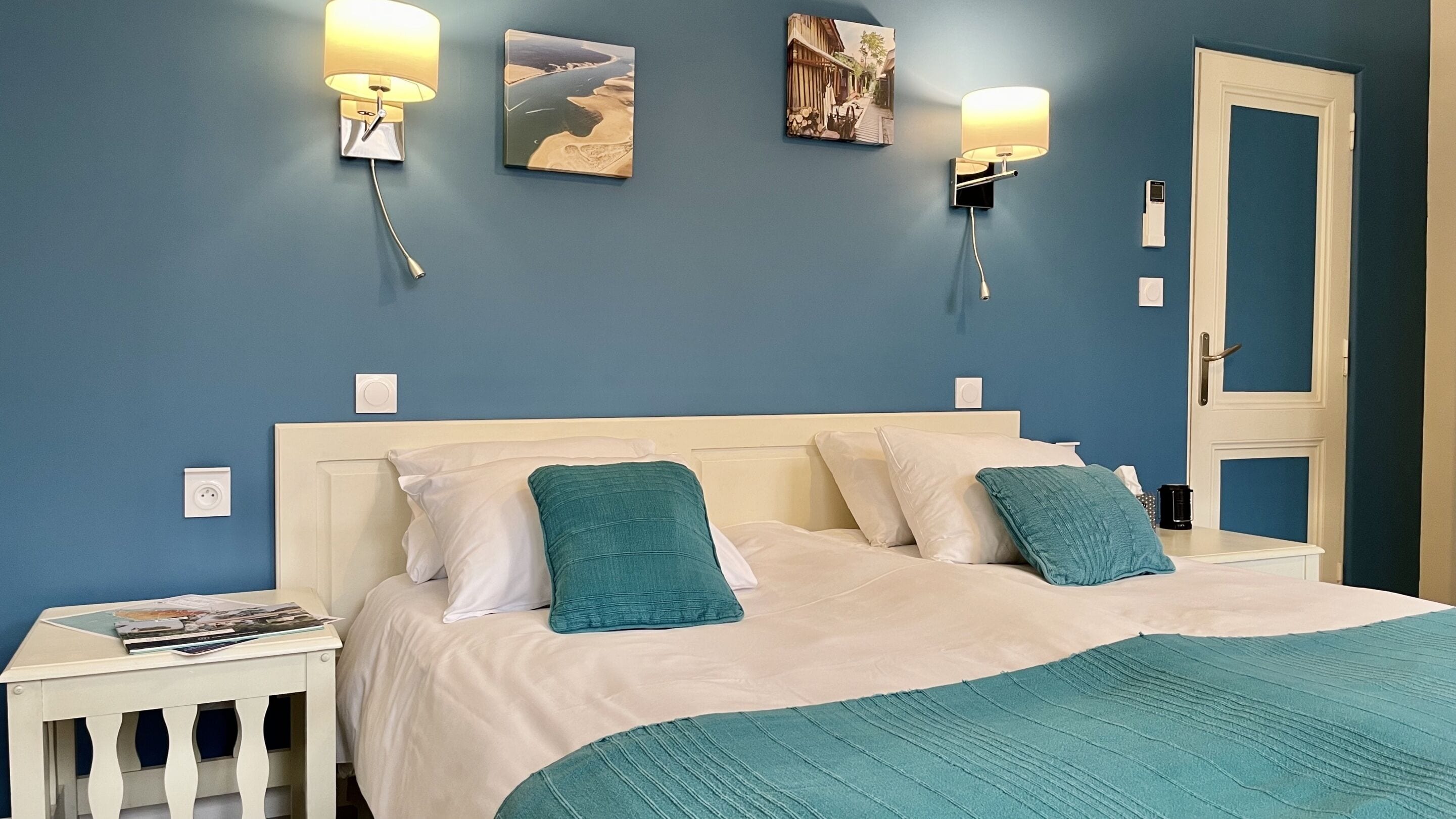 A bedroom with a bed, two wall-mounted lamps, and two framed pictures on the wall.