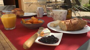 A breakfast table with a glass of orange juice, a bowl of fruit, a croissant, cheese, and a baguette.