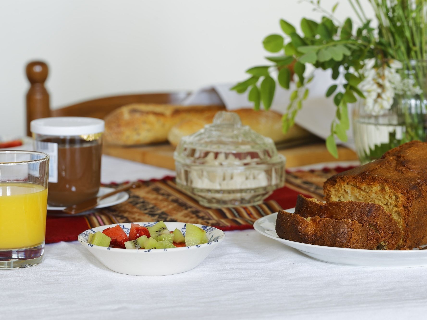 Un desayuno con pan, un vaso de zumo de naranja, un bol de fruta y un tarro de miel.