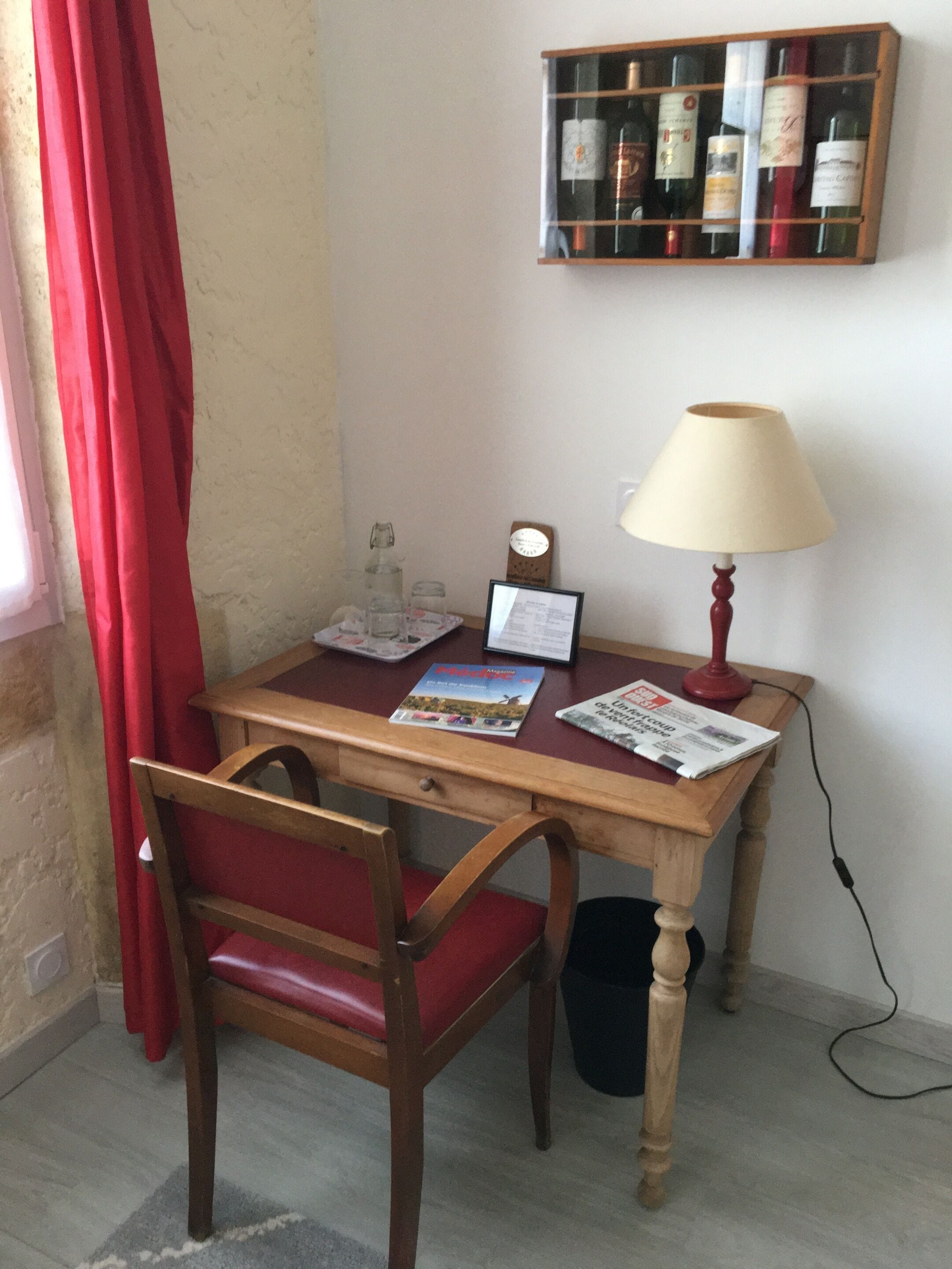 A wooden desk with a red chair, a lamp, and a wine rack above it.