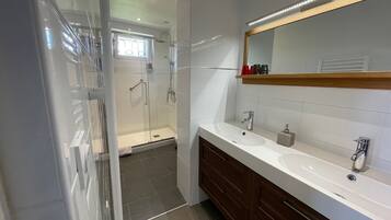 Een moderne badkamer met een douchecabine van glas, een wastafel met spiegel en een wasbak.