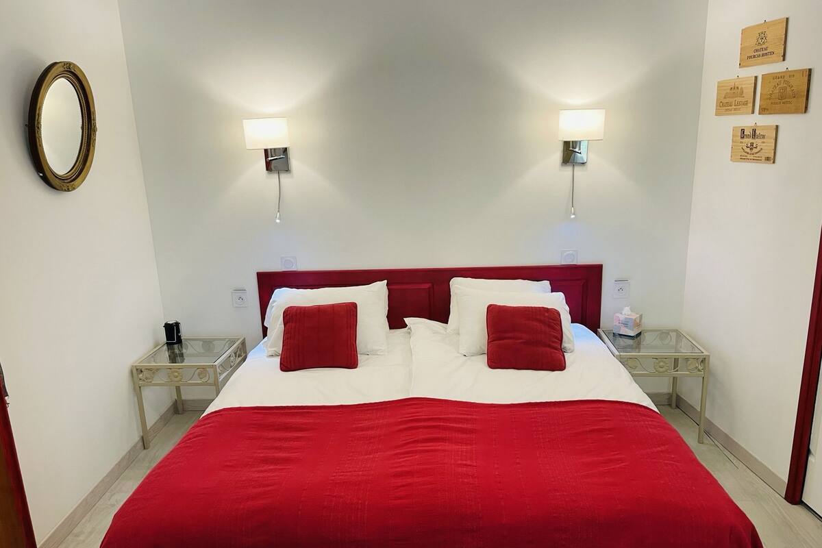 Habitación de hotel con una cama grande, dos mesitas de noche, un espejo y lámparas de pared.