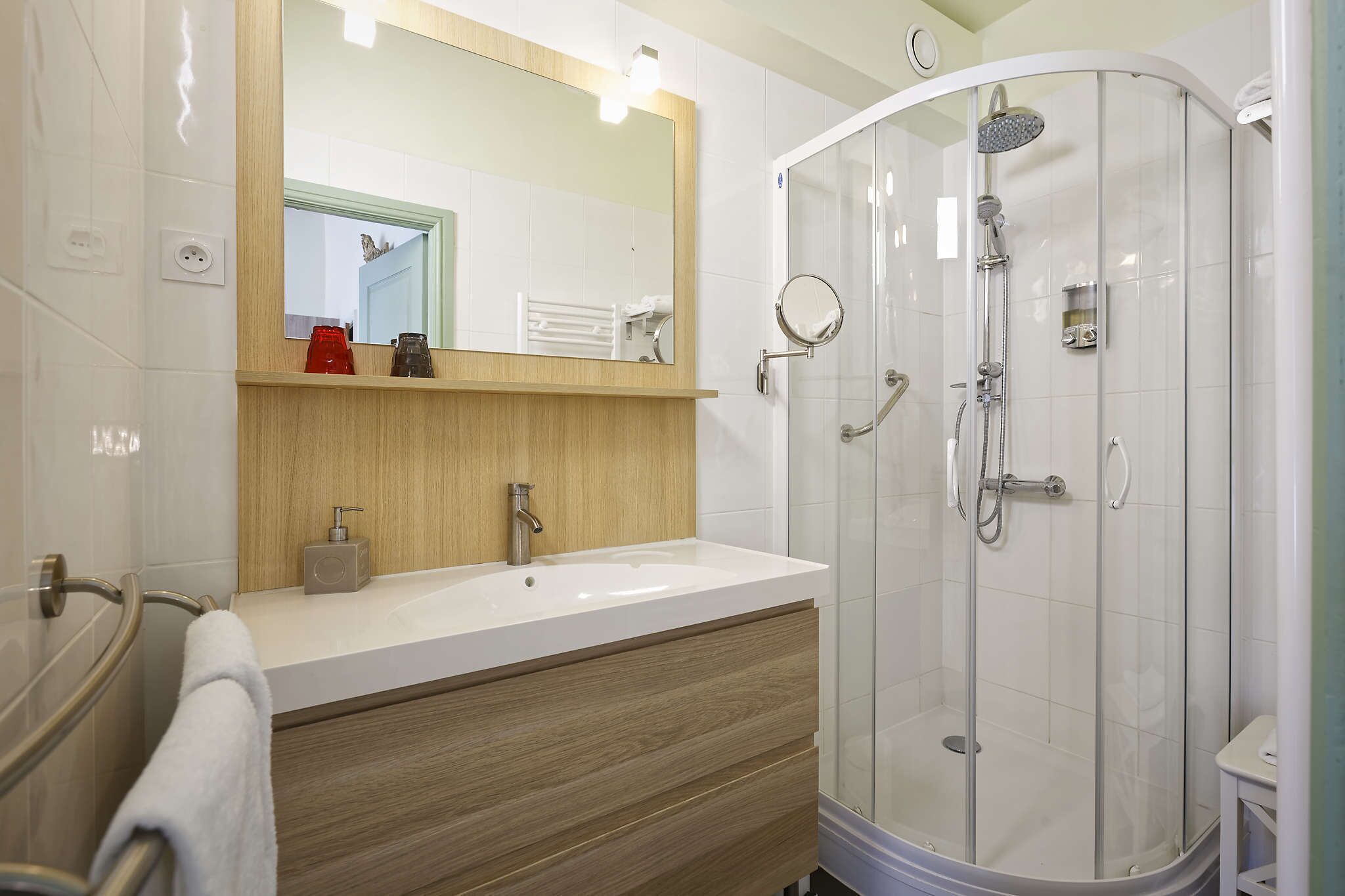 A modern bathroom with a white sink, wooden vanity, a glass shower enclosure, and a mirror above the sink.