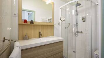 A modern bathroom with a white sink, wooden vanity, a glass shower enclosure, and a mirror above the sink.