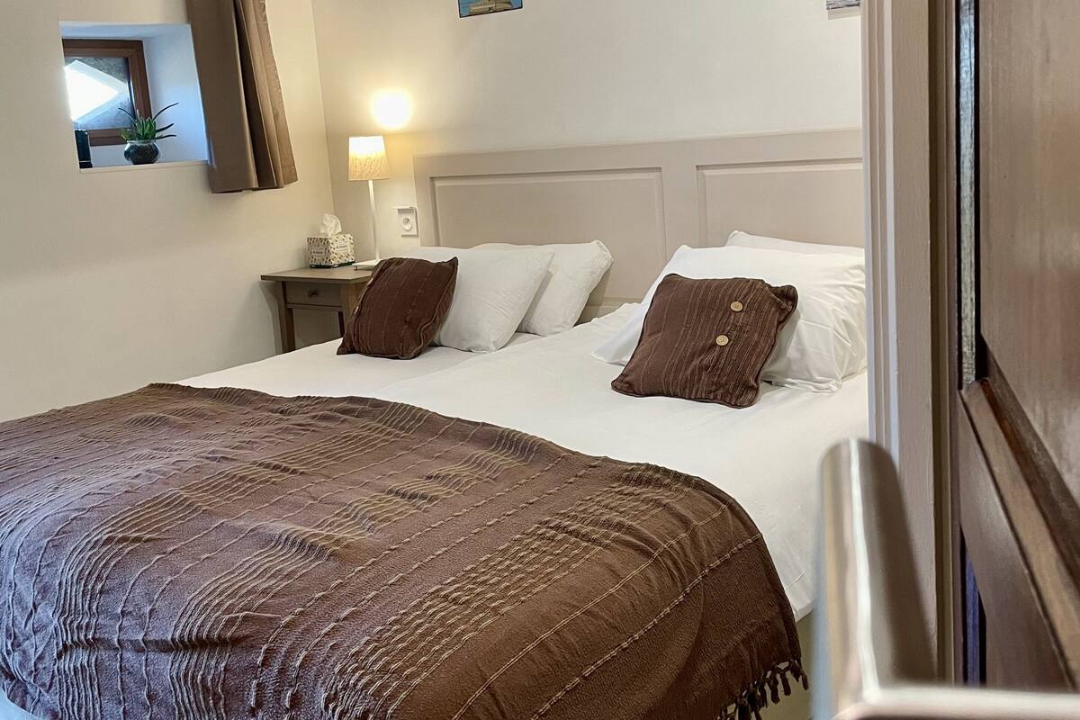 Habitación de hotel con una cama grande, una mesita de noche con lámpara, una planta pequeña y un cuadro en la pared.