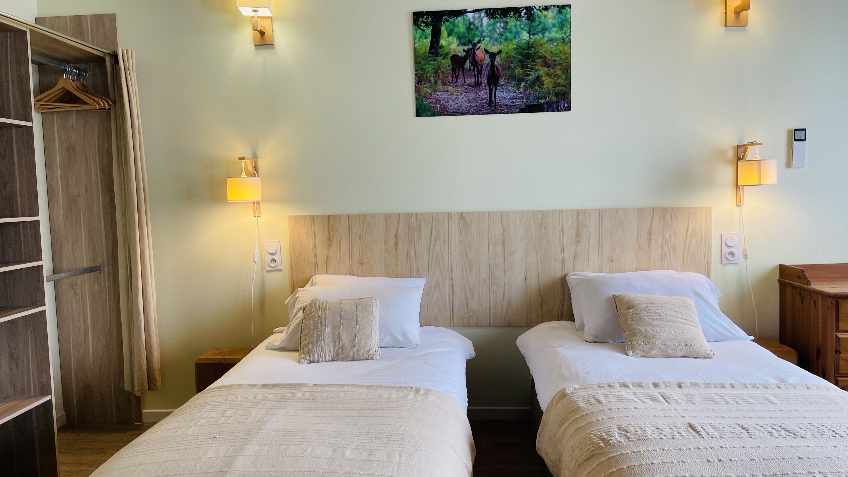 A hotel room with two beds, wooden headboards, and a forest-themed wall art.