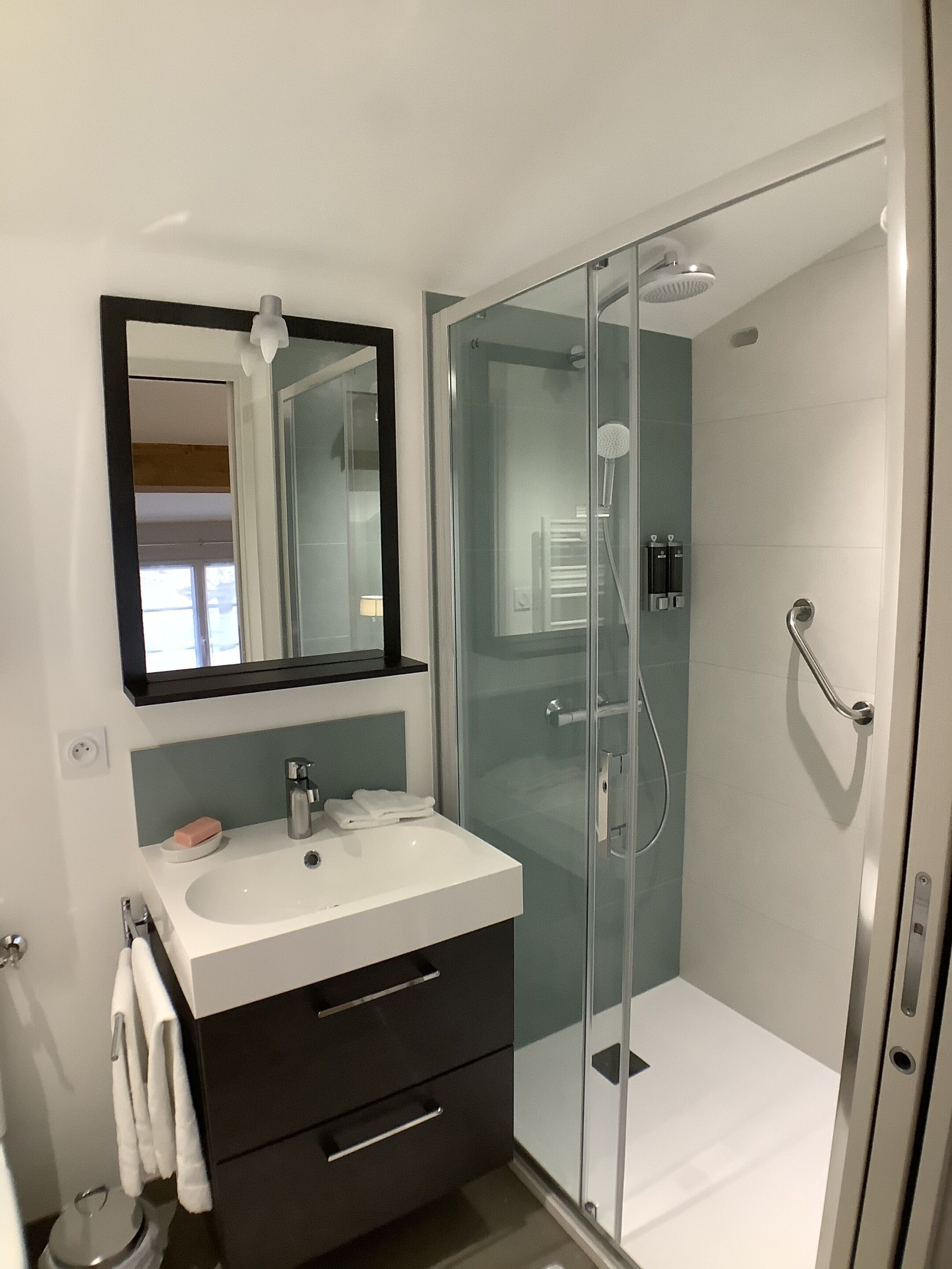 A modern bathroom with a glass-enclosed shower, a white sink, and a dark vanity.