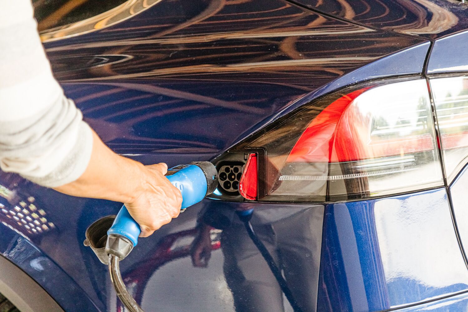 A person charging a car with a blue charging cable.