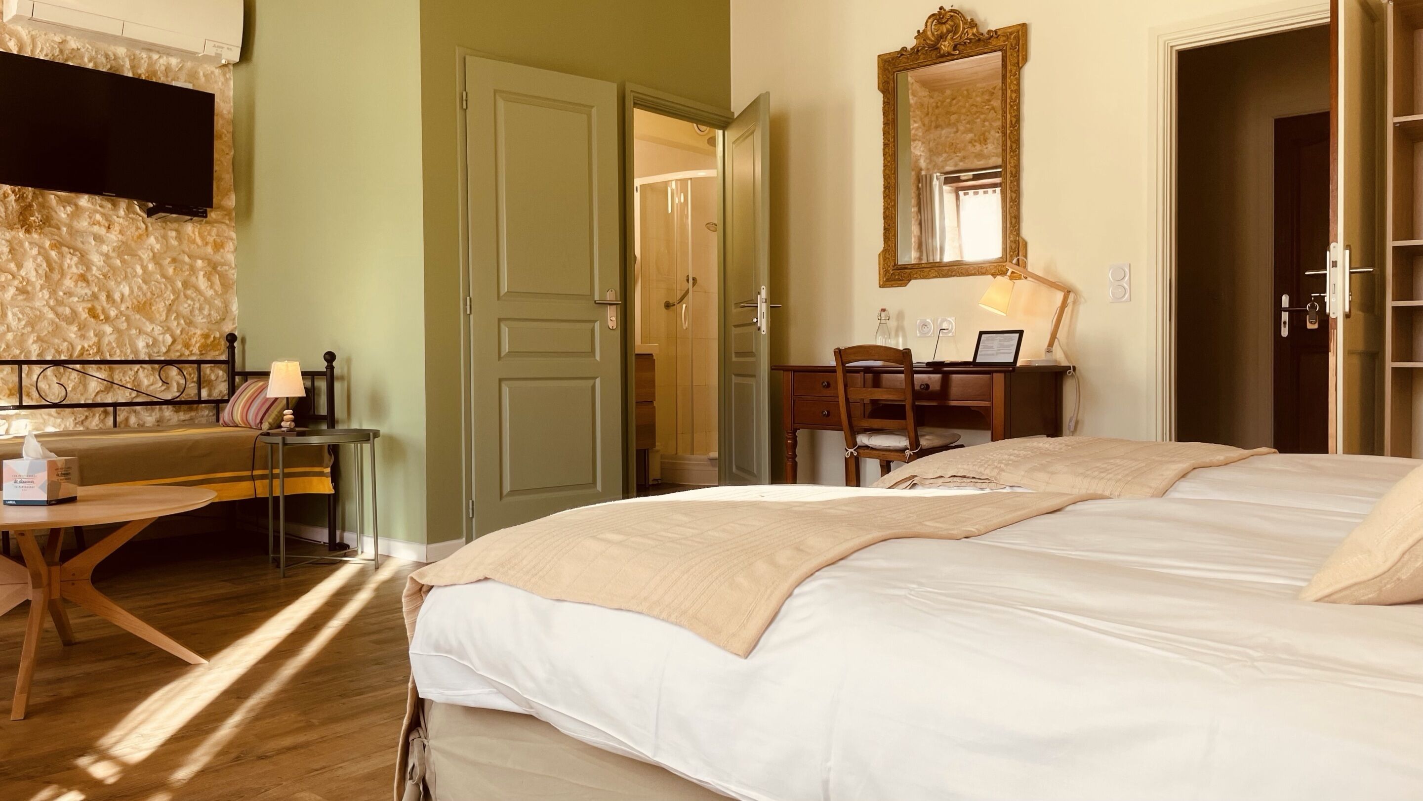 A hotel room with a bed, a desk, a chair, a mirror, and a door leading to a bathroom.