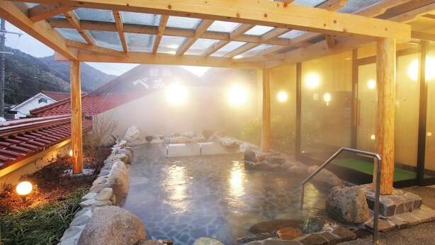 A hot spring bath area with a wooden pergola, stone pathway, and a view of a mountain in the background.