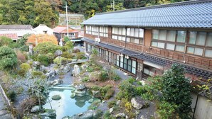 A traditional Japanese building with a wooden exterior and tiled roof, surrounded by a garden with a pond and rocks.