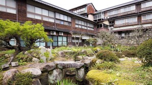A traditional Japanese building with a garden featuring rocks, a small pond, and pine trees.