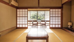 A traditional Japanese room with tatami flooring, a low table, two chairs, and a view through a shoji screen.