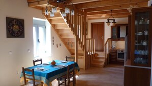 A dining area with a wooden staircase, a kitchen with glass cabinets, and a clock on the wall. - Viva Elafonisi (Kissamos)