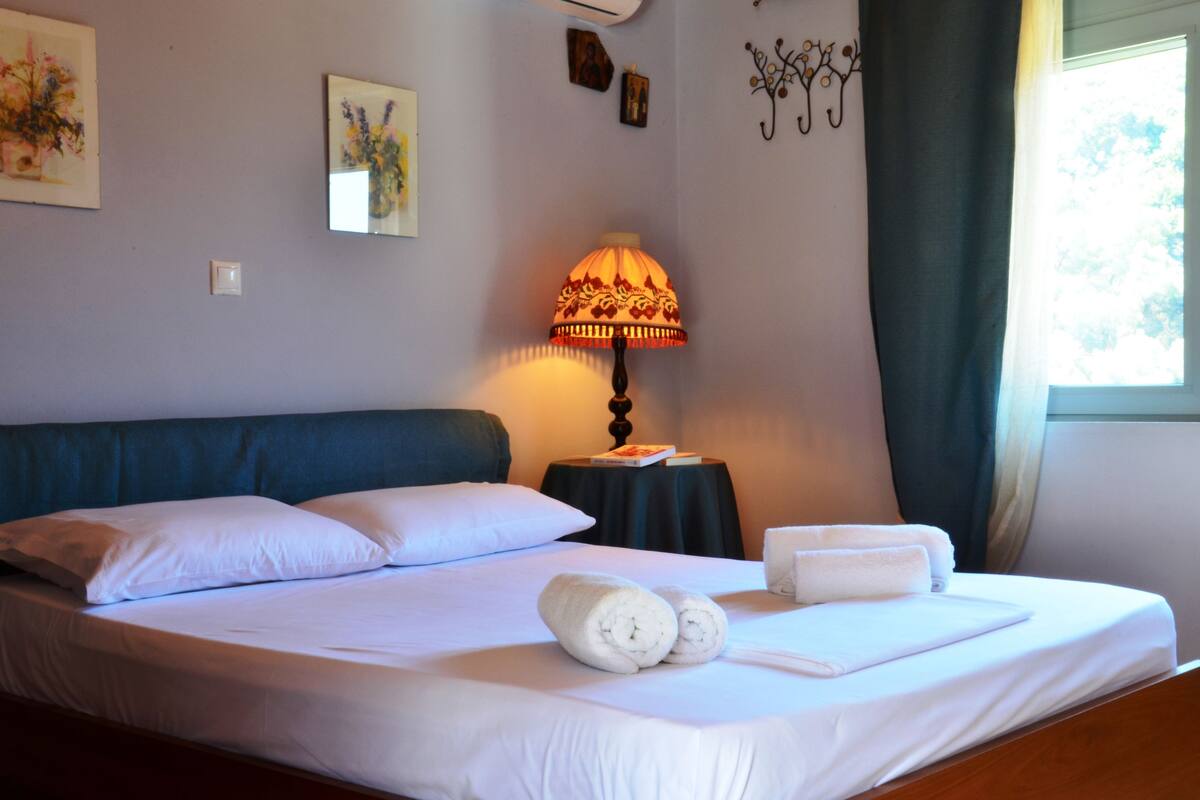 Een opgemaakt bed met witte lakens, een nachtkastje met een lamp en kunst aan de wanden.