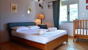 A bedroom with a wooden bed, a bedside lamp, a crib, and a window with curtains. - Viva Elafonisi (Kissamos)