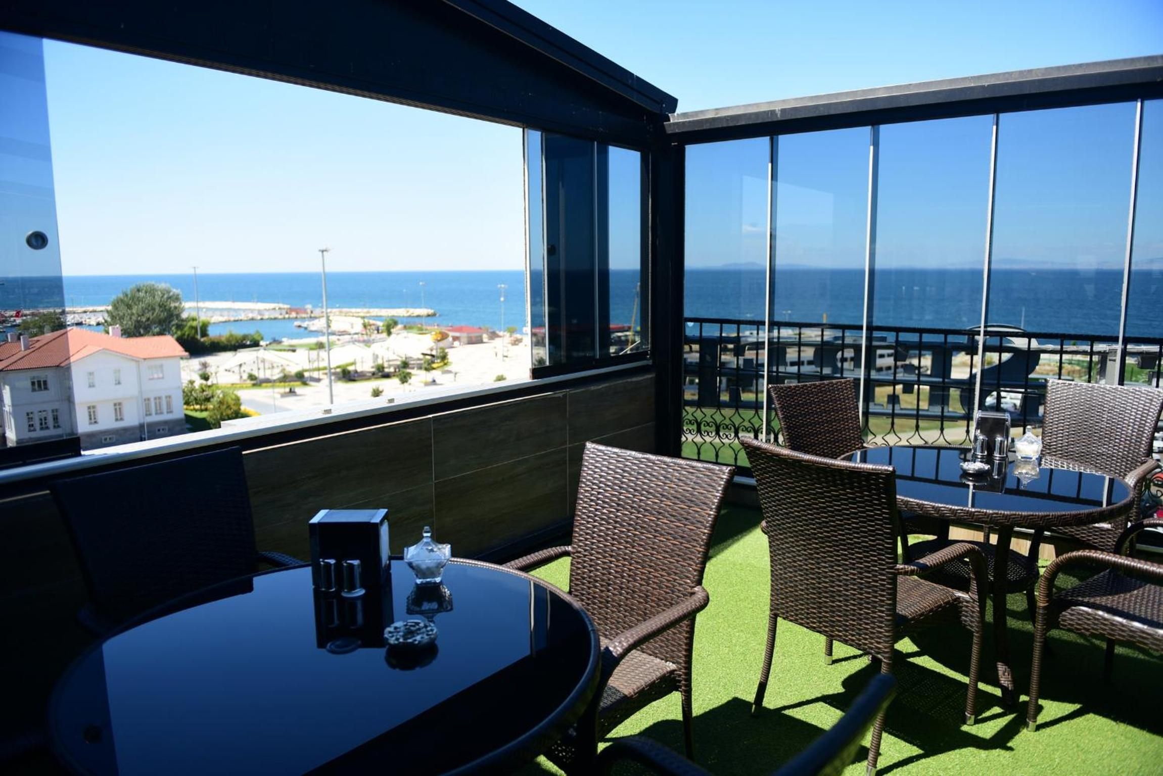 Een balkon met een tafel en stoelen, met uitzicht op de kust, gebouwen en een pier.