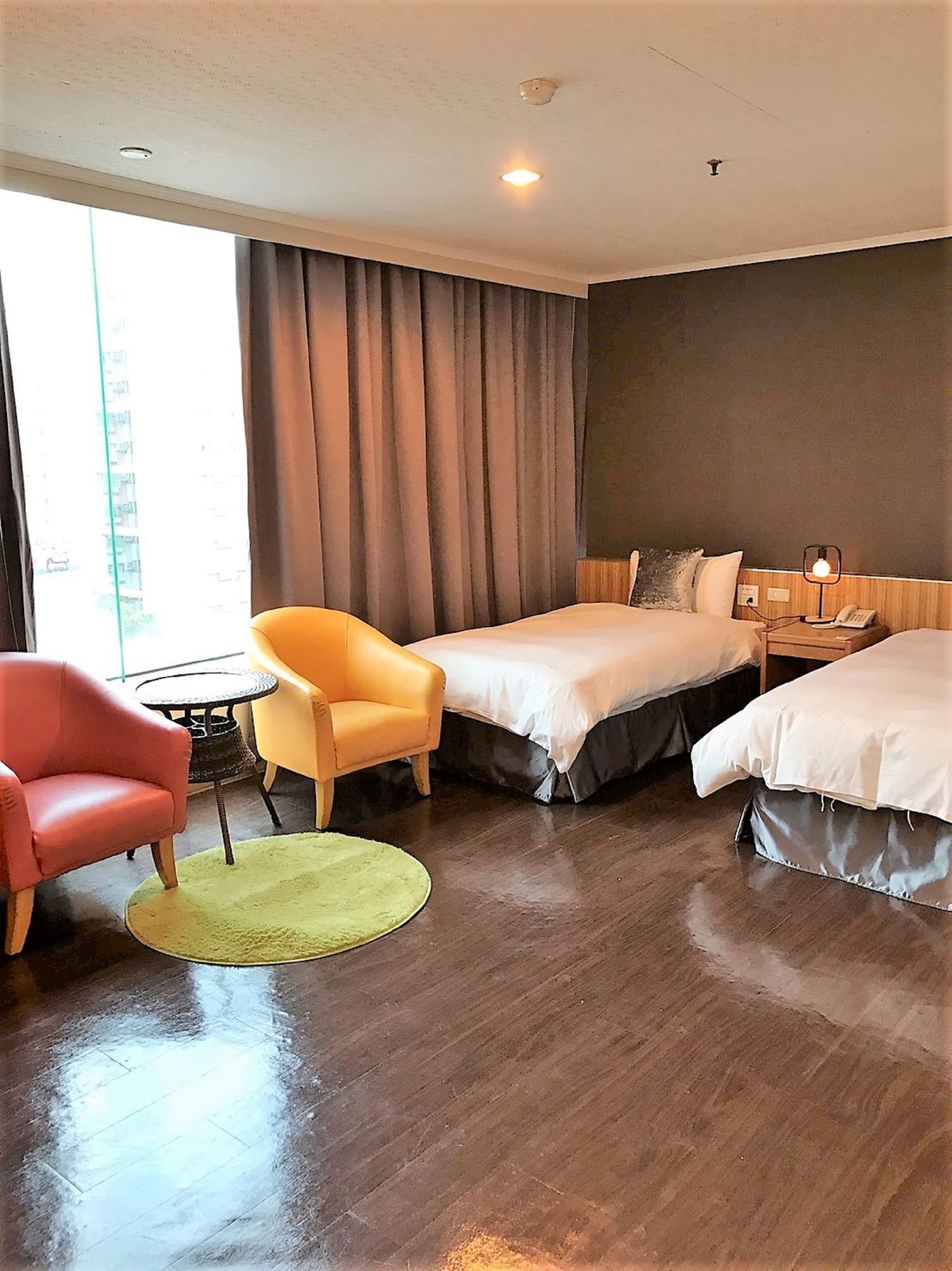 Habitación de hotel con dos camas, una silla roja, una amarilla y una pequeña mesa con una lámpara.