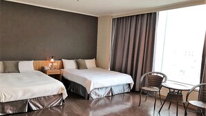 A hotel room with two beds, a small table with chairs, a nightstand with a lamp, and a large window with curtains. - Nanka Express Hotel (Chiayi City)