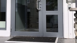Una entrada moderna de edificio con puerta de vidrio, sistema de entrada por teclado y un escalón de piedra que lleva a la puerta.