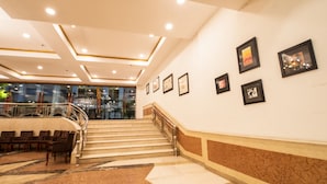 A hotel lobby with a staircase, seating area, and framed pictures on the wall. - Hotel Celebration Gardens (New Delhi)