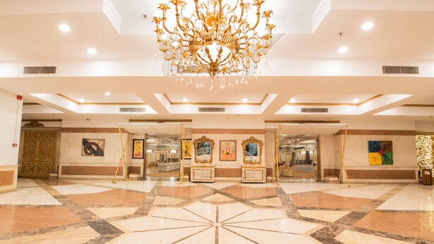 A spacious lobby with a large chandelier, marble flooring, and framed artwork on the walls. - Hotel Celebration Gardens (New Delhi)