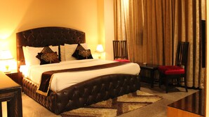 A hotel room with a large bed, a desk, a chair, and a lamp. - Karan Holidays (New Delhi)