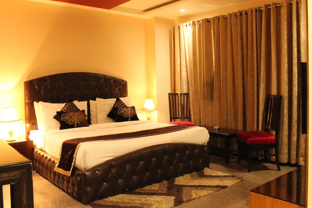 A hotel room with a large bed, a desk, a chair, and a lamp.