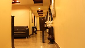 A hotel hallway with a black leather sofa, a vase with white flowers, and framed pictures on the walls. - Karan Holidays (New Delhi)