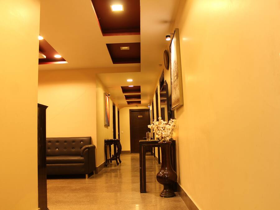 A hotel hallway with a black leather sofa, a vase with white flowers, and framed pictures on the walls.