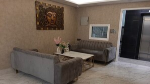 A modern living room with two grey sofas, a marble floor, a coffee table with flowers, a wall-mounted artwork, and a window with blinds. - Karan Holidays (New Delhi)