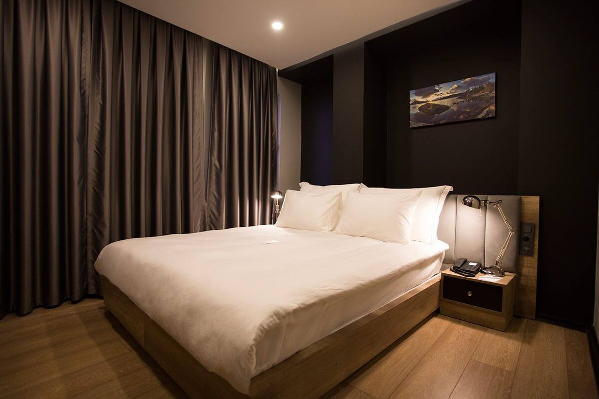 A modern hotel room with a large bed, a nightstand with a lamp, and a painting on the wall.