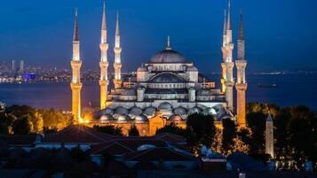A grand mosque with multiple minarets and a large central dome, surrounded by water and urban skyline.