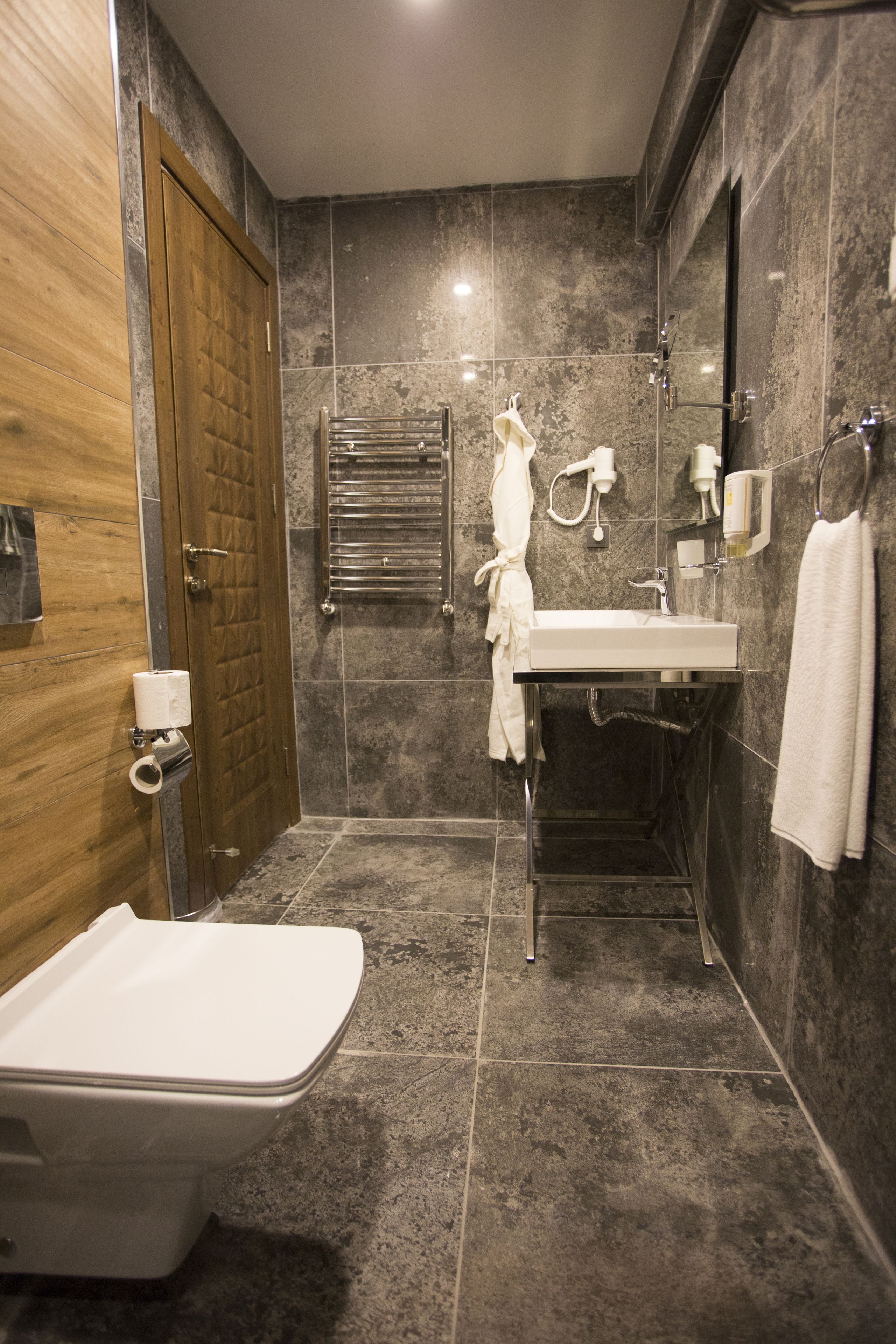 A modern bathroom with a wooden door, a white bathtub, a sink, and a towel rack.