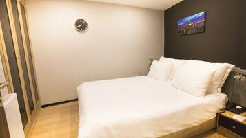 Habitación de hotel con cama, mesita de noche, reloj de pared y una pintura de un paisaje urbano.