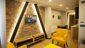 A modern living room with a brick wall, a flat-screen TV, yellow chairs, and a wooden coffee table. - Long Stay Istanbul (Istanbul)