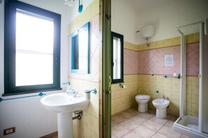 Een badkamer met een wastafel, twee toiletten, een douche en een raam.