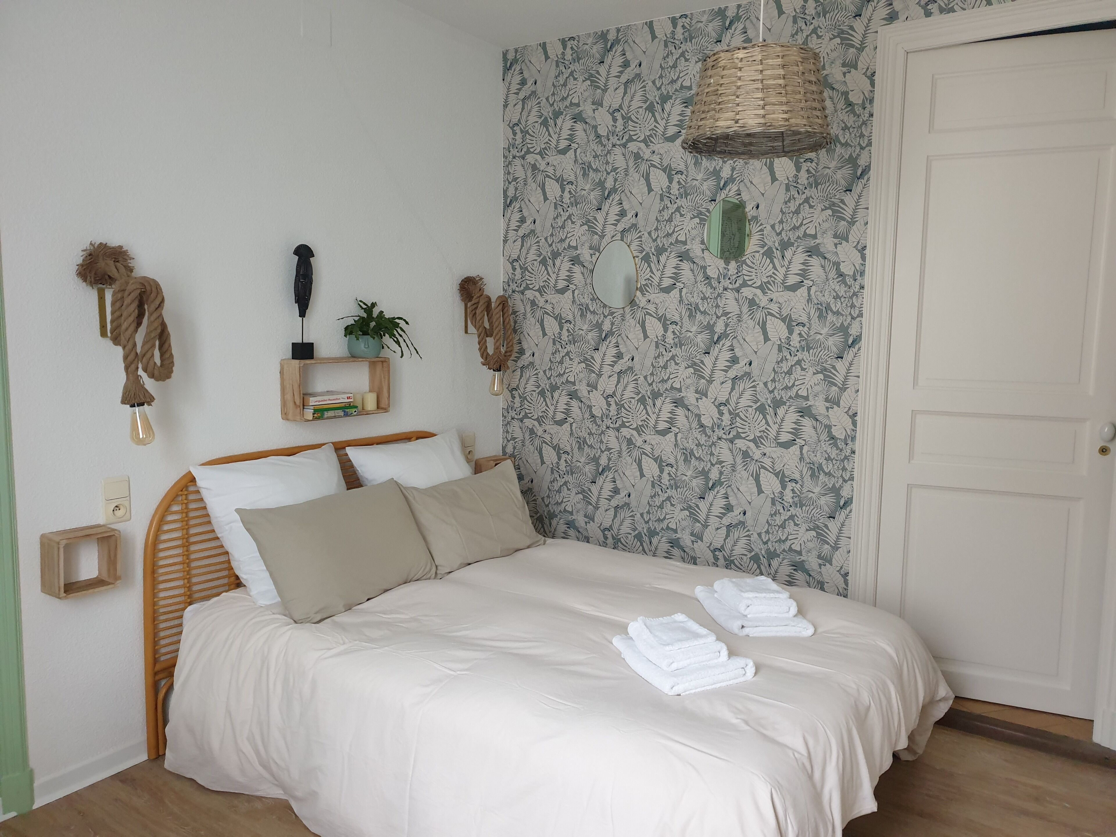 A neatly made bed with white linens, a bedside table with a lamp, and a wall with a leafy pattern.