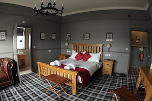 Un dormitorio con suelo a cuadros, una cama de madera con almohadas rojas, un sillón de cuero y una pequeña mesa de madera.