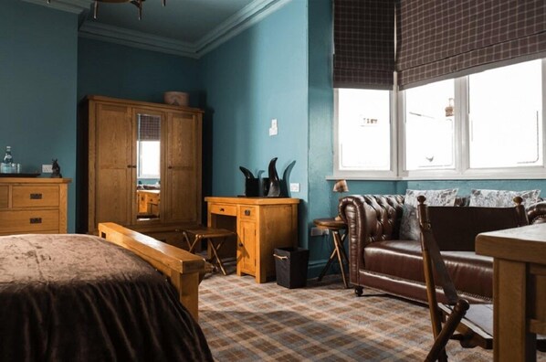 Una habitación con un armario grande de madera, un sofá de cuero, un escritorio de madera y una alfombra estampada.