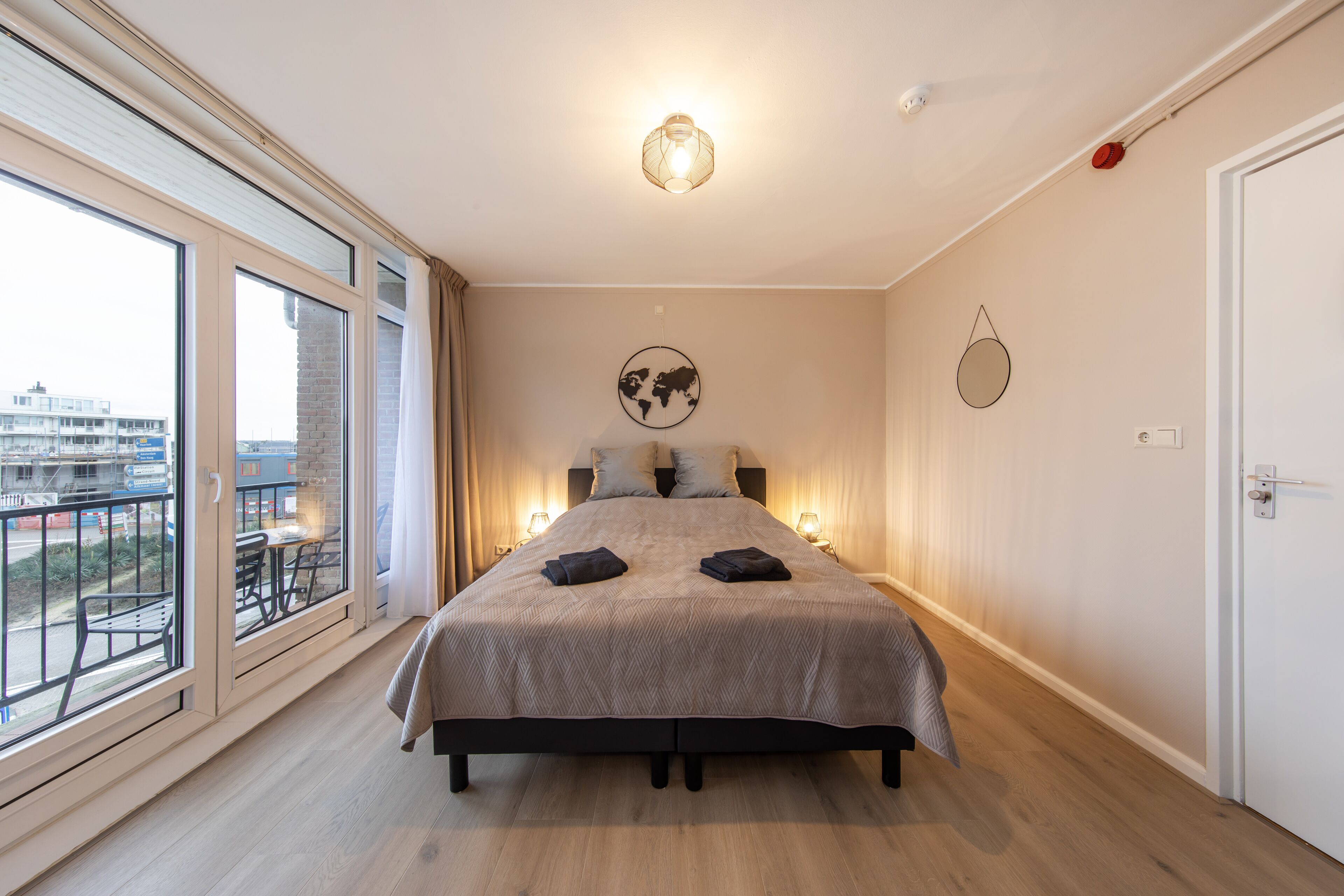 Un dormitorio con una cama grande, vistas de la ciudad desde un balcón y un mapa del mundo en la pared.