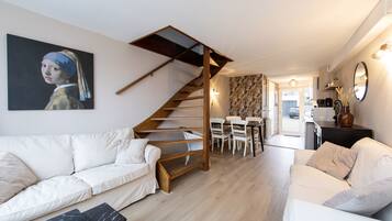 Uma sala de estar moderna com um sofá branco, uma escada de madeira e uma área de jantar.