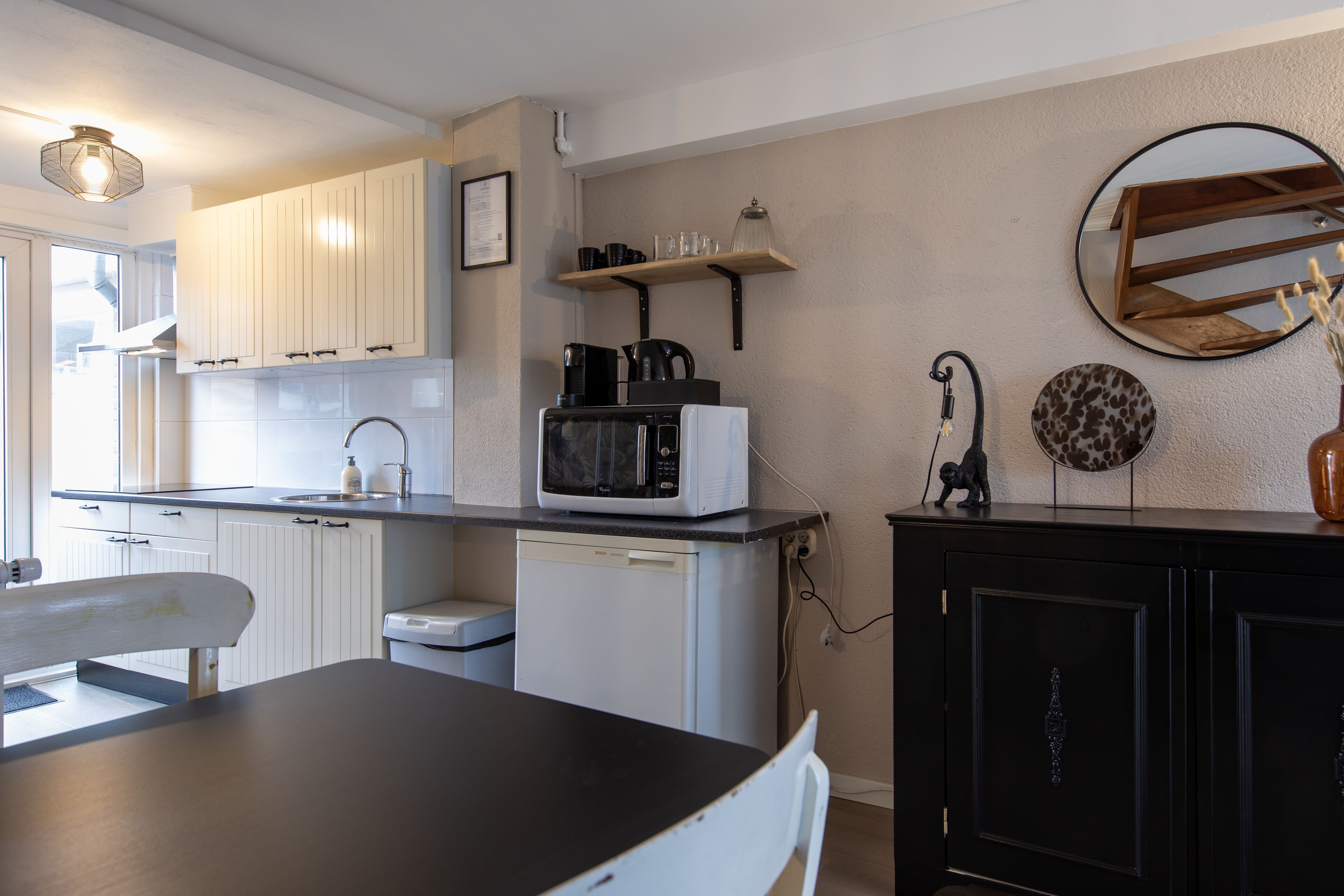 A compact kitchen with white cabinets, a microwave, a small dishwasher, and a black countertop.