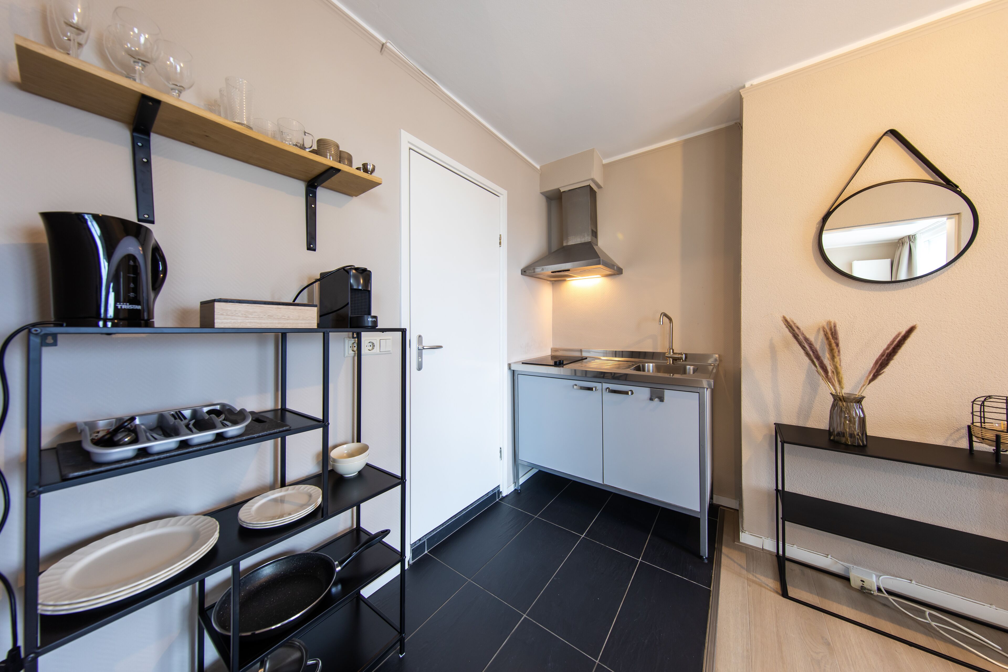 A compact kitchen with black and white appliances, a coffee maker, and a mirror on the wall.