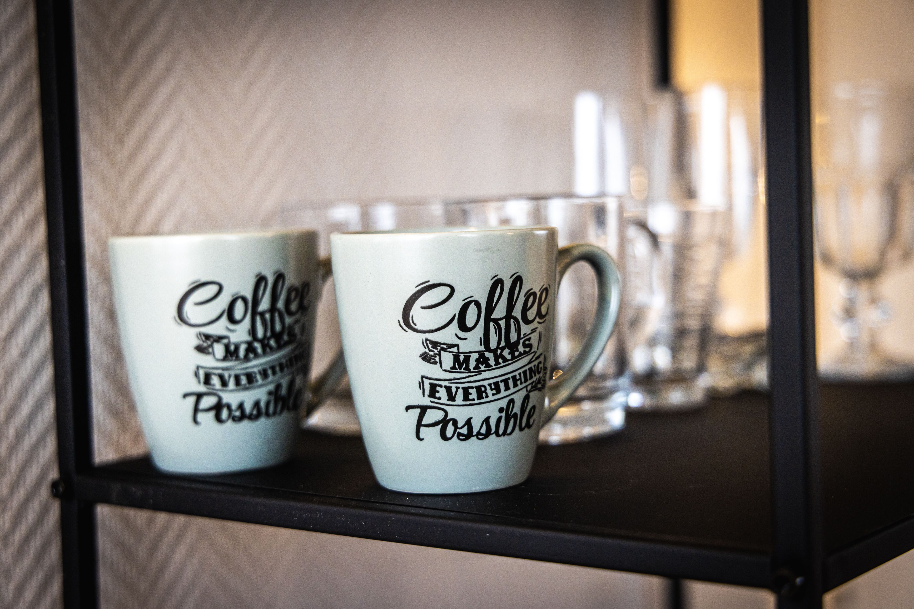Two coffee mugs with motivational text on a shelf.