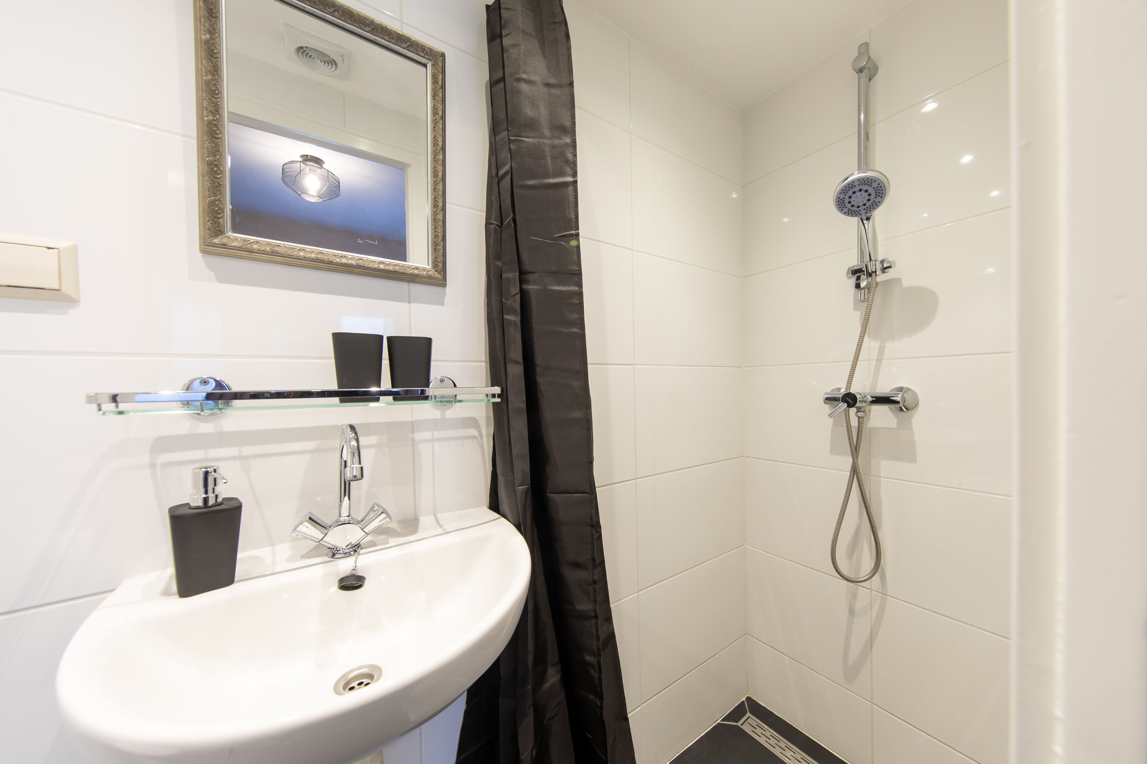 A bathroom with a sink, mirror, shower, and a glass shelf with toiletries.