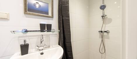 A bathroom with a sink, mirror, shower, and a glass shelf with toiletries.