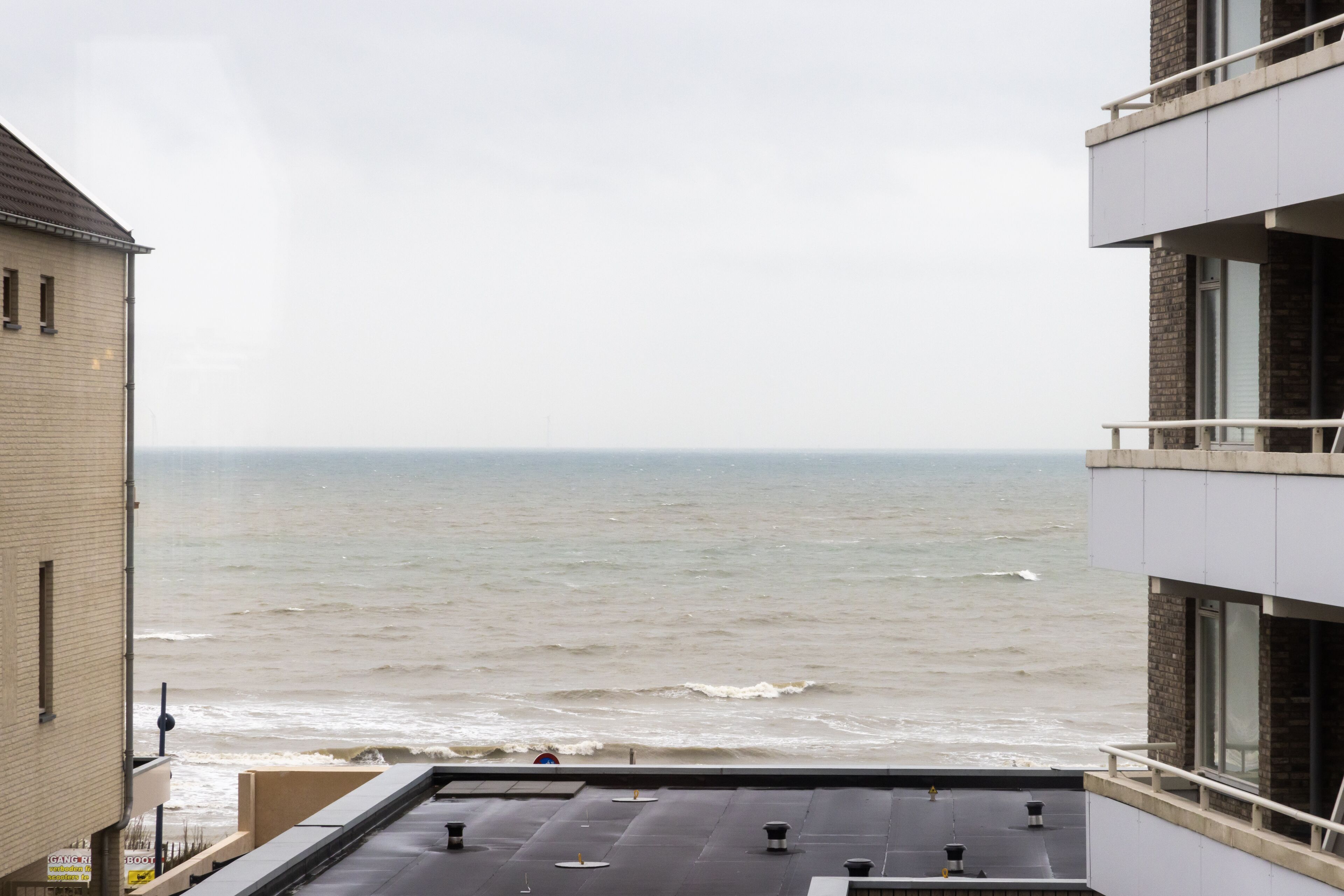 A view of the sea from a building's rooftop, featuring a flat roof with several vents and a railing.